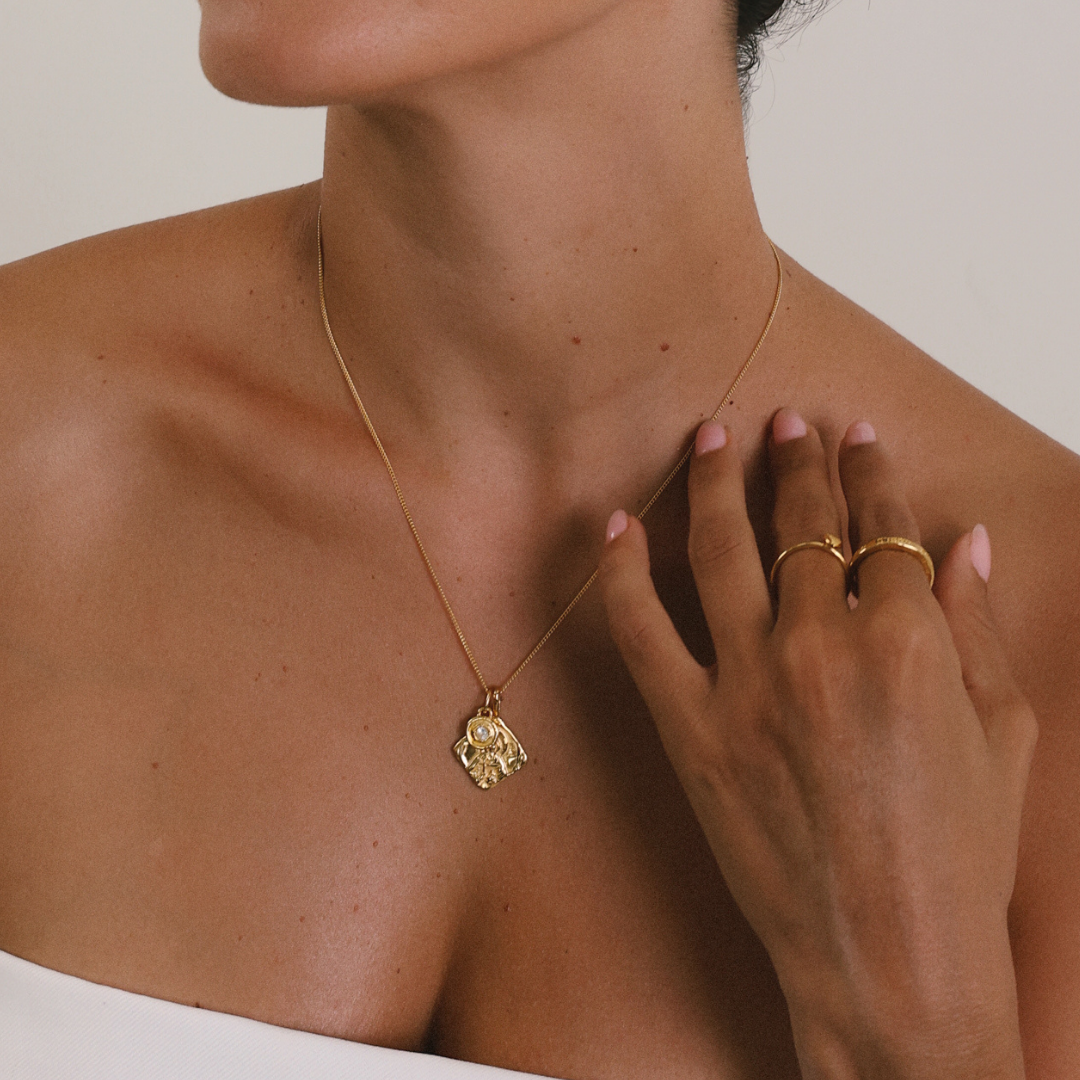 Gold necklace with a pendant worn by a person, with a hand touching the neck.