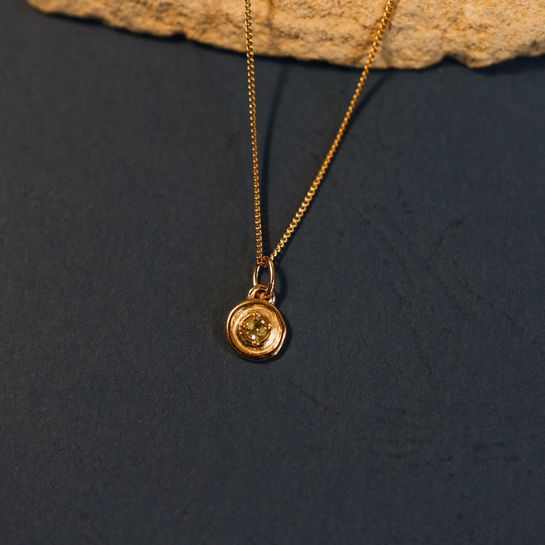 Gold necklace with a round pendant on a dark surface
