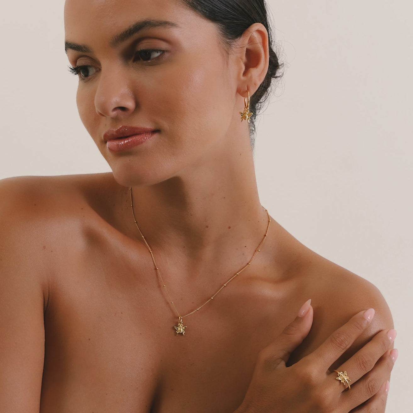 Woman wearing gold jewelry including a necklace, ring, and bracelet on a plain background