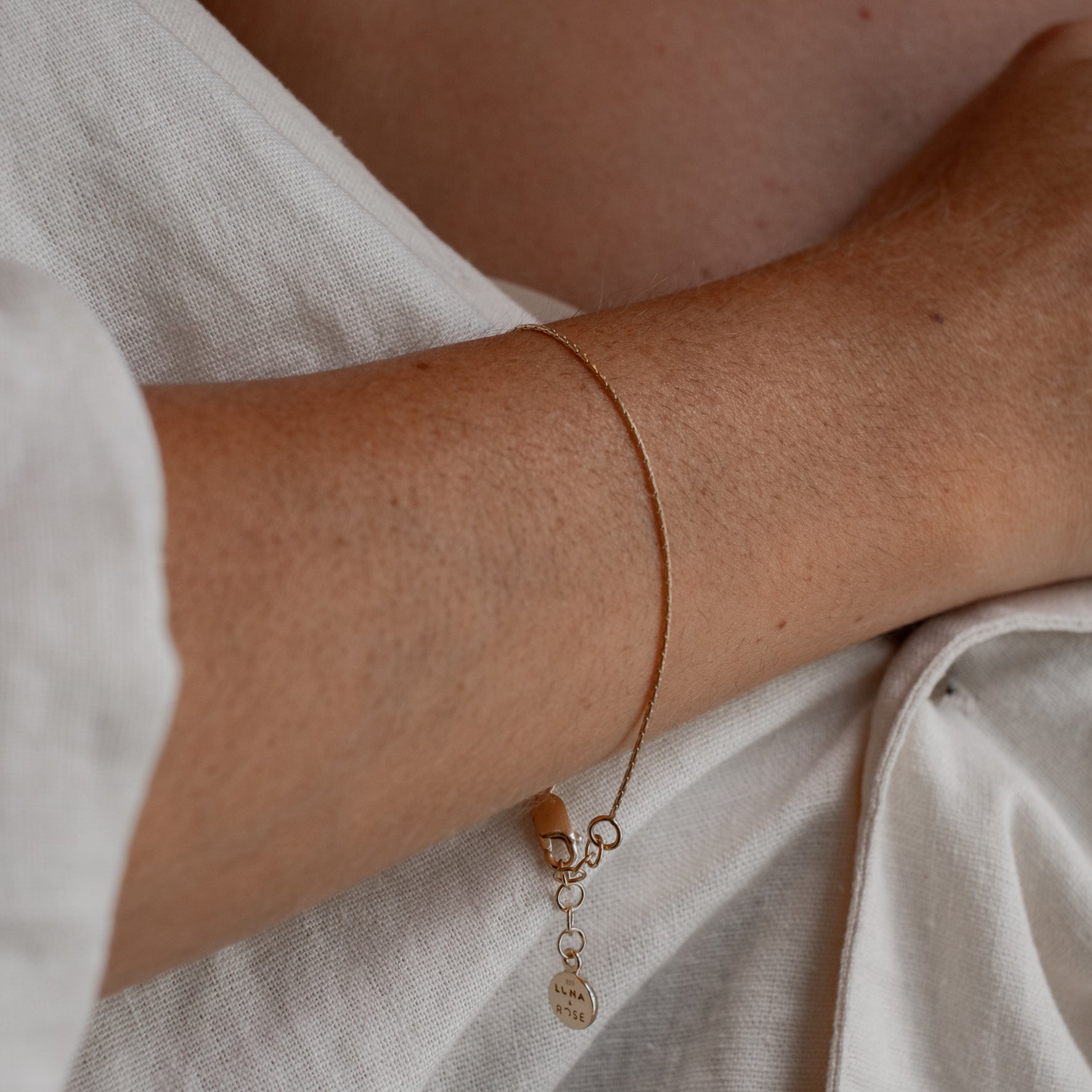 Close-up of a woman wearing a gold bracelet, paired with a white blouse