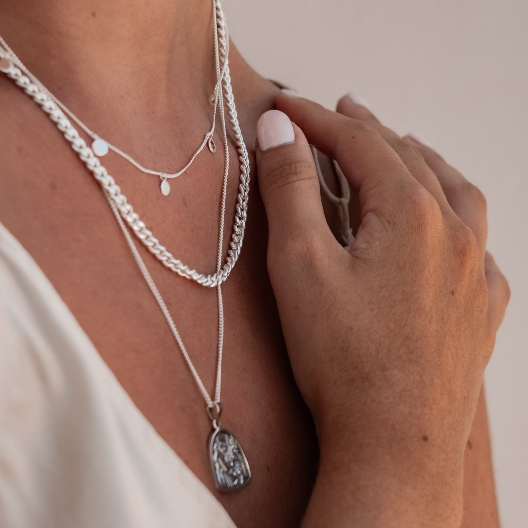 A woman with brown hair wearing 2 silver necklaces holding her hand on her shoulder