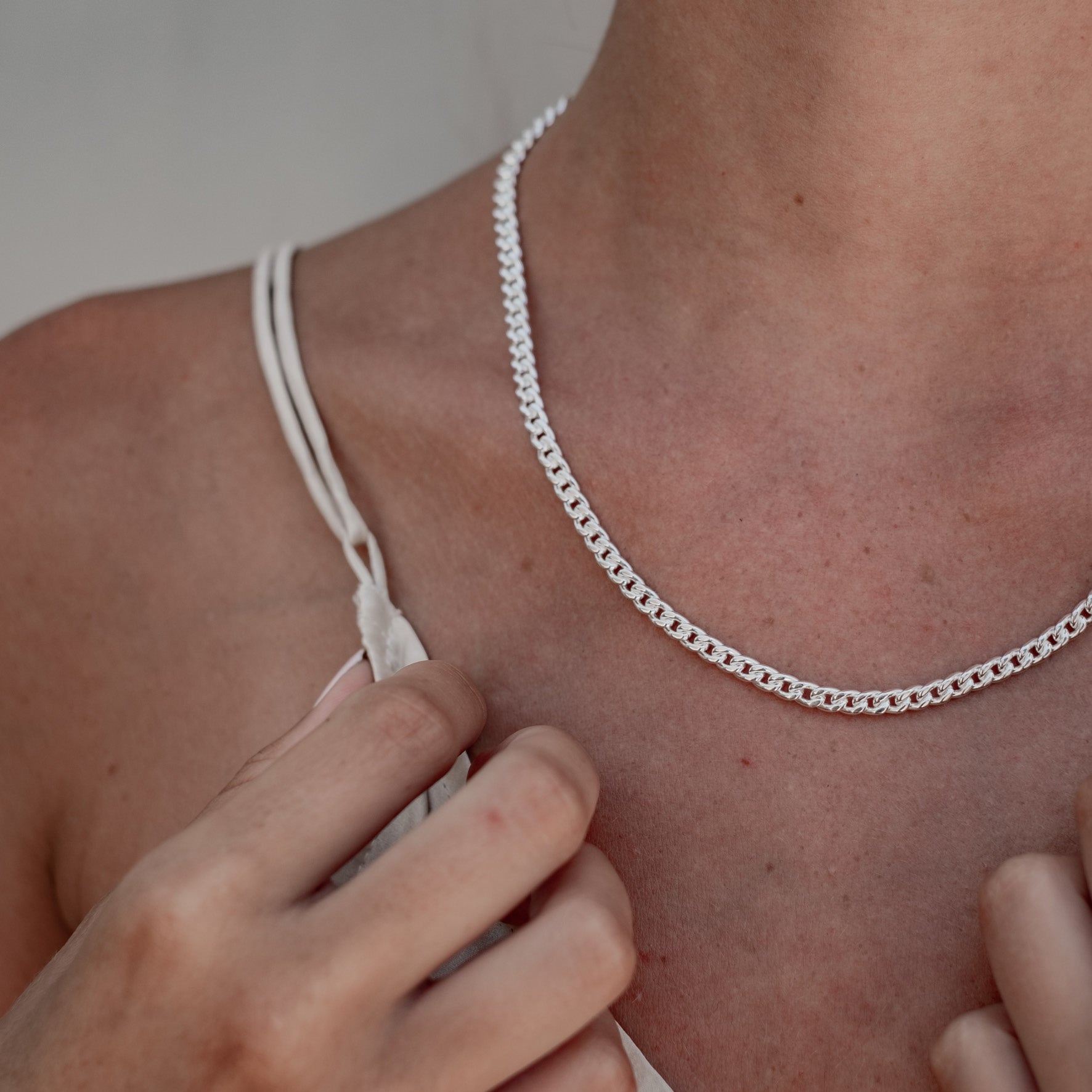 Close-up of a woman wearing a single silver chain necklace with flat and interlocking links