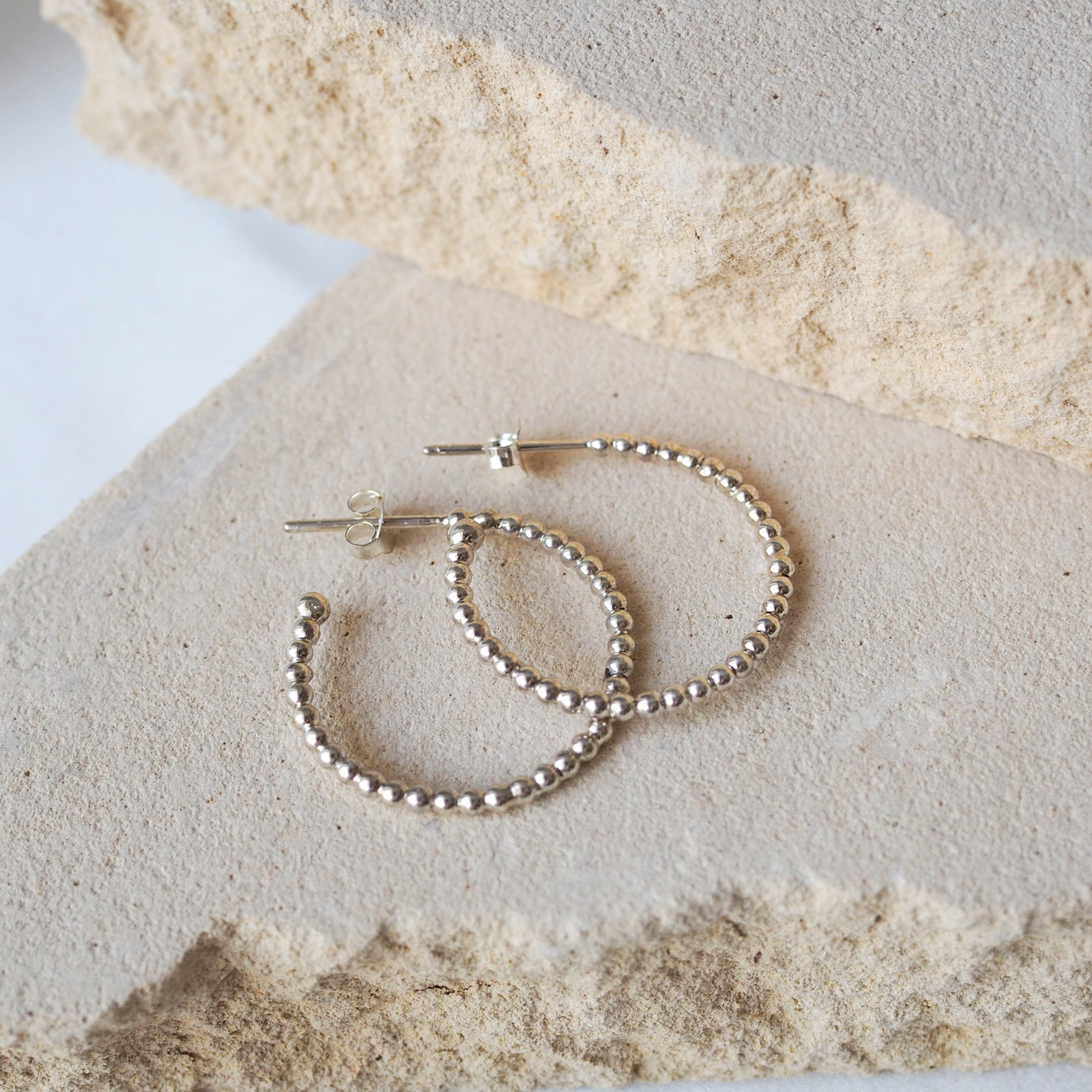 Silver beaded earrings displayed on a textured beige stone