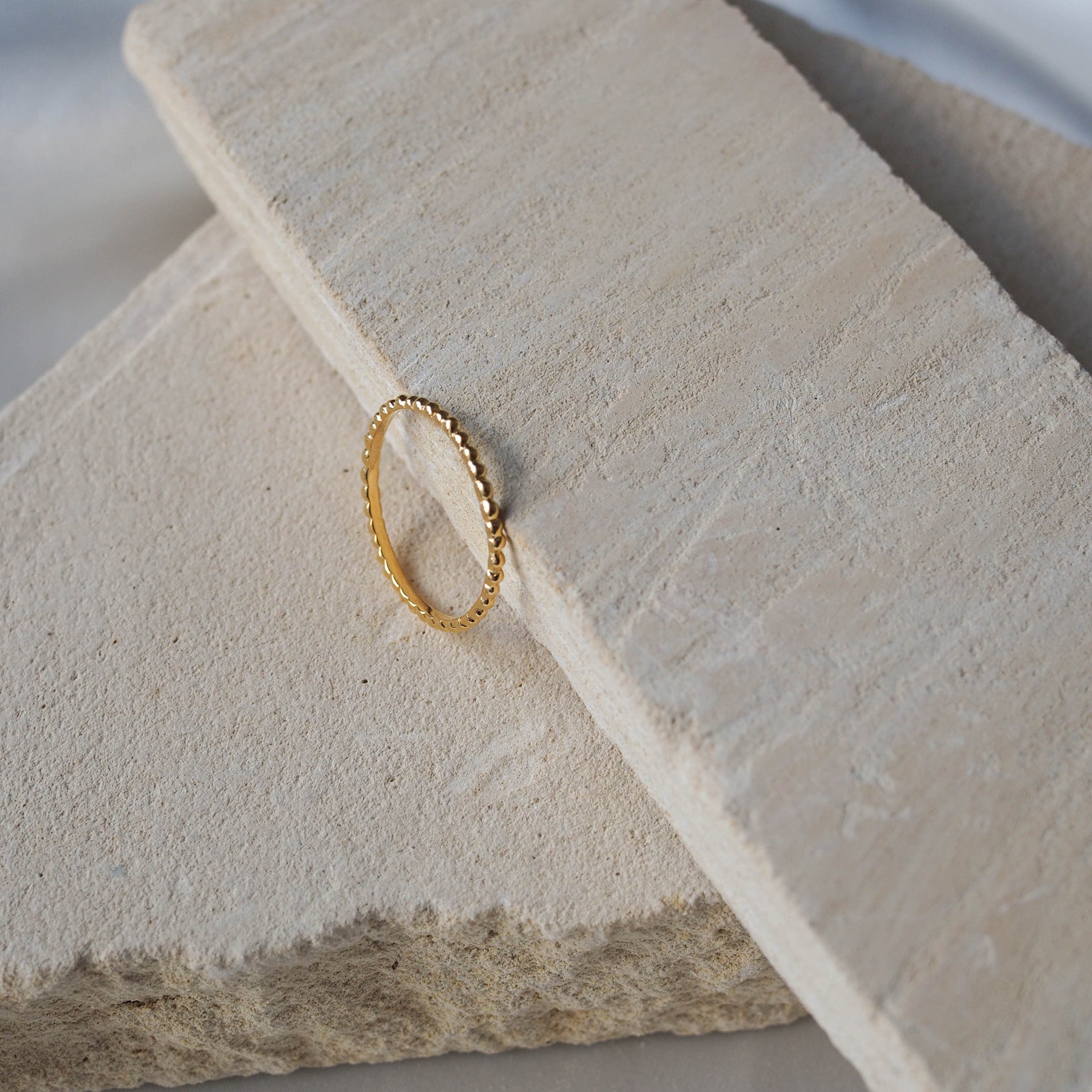 Gold beaded ring displayed on a textured beige stone.