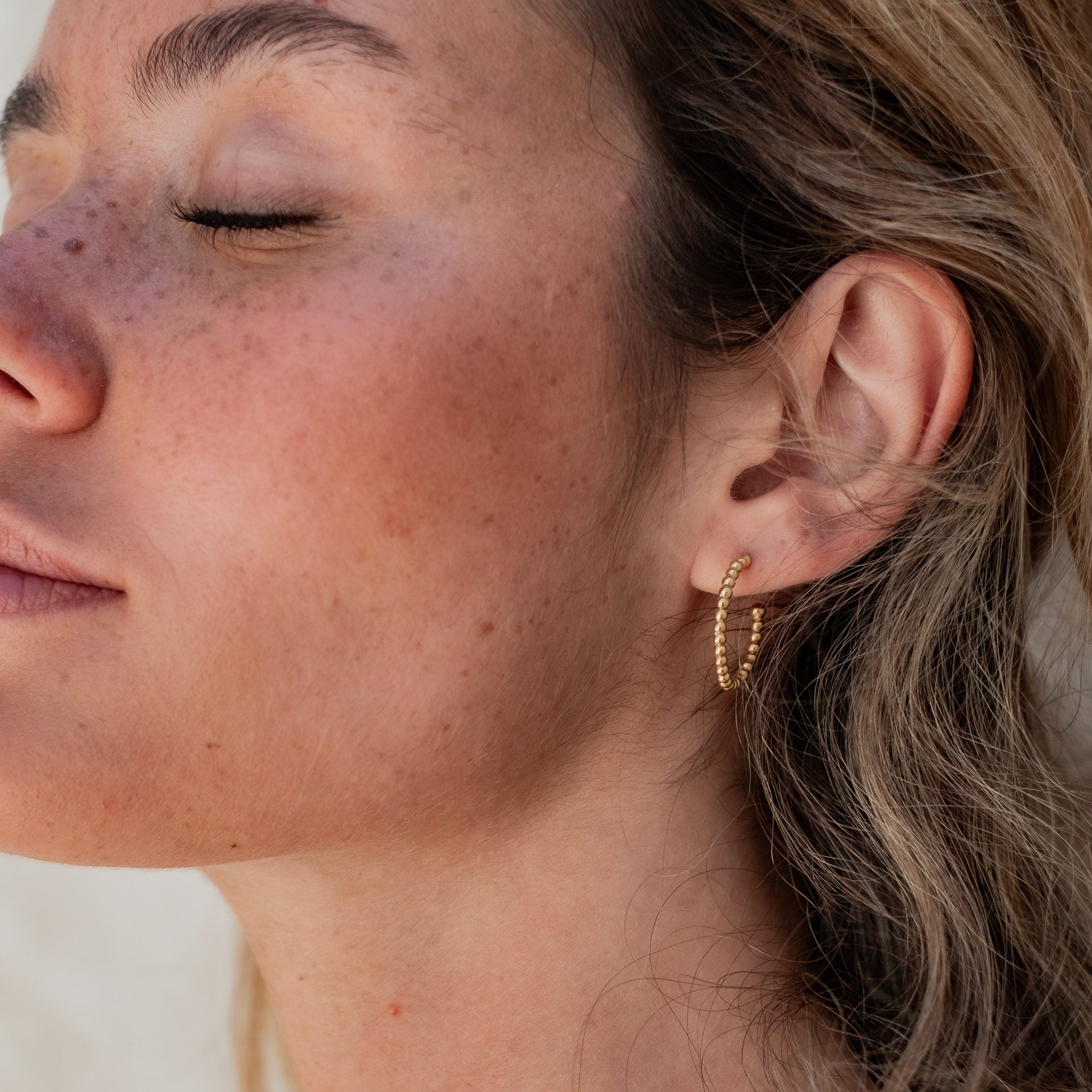 Close-up of a woman wearing one gold beaded earing