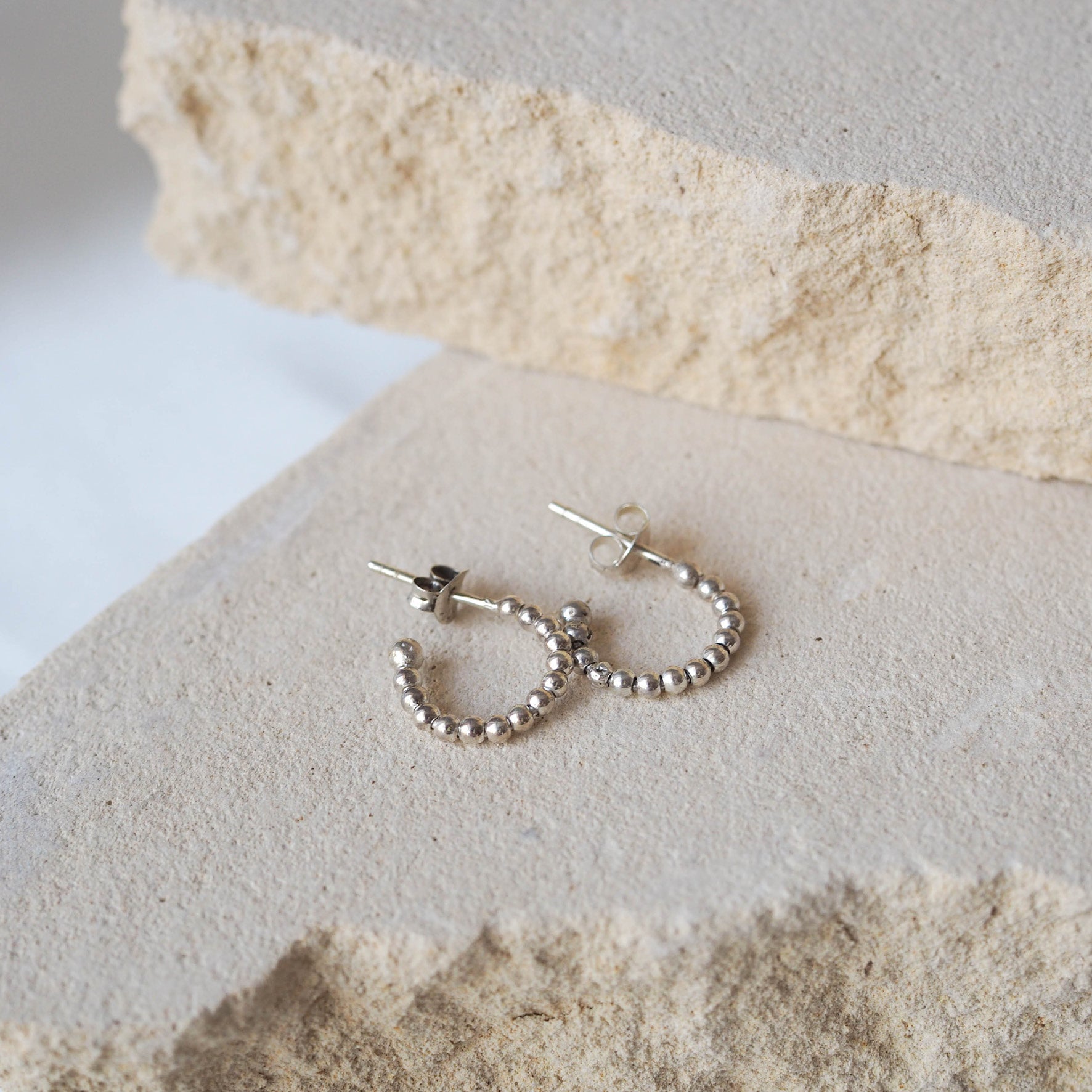 Silver beaded earrings displayed on a textured beige stone