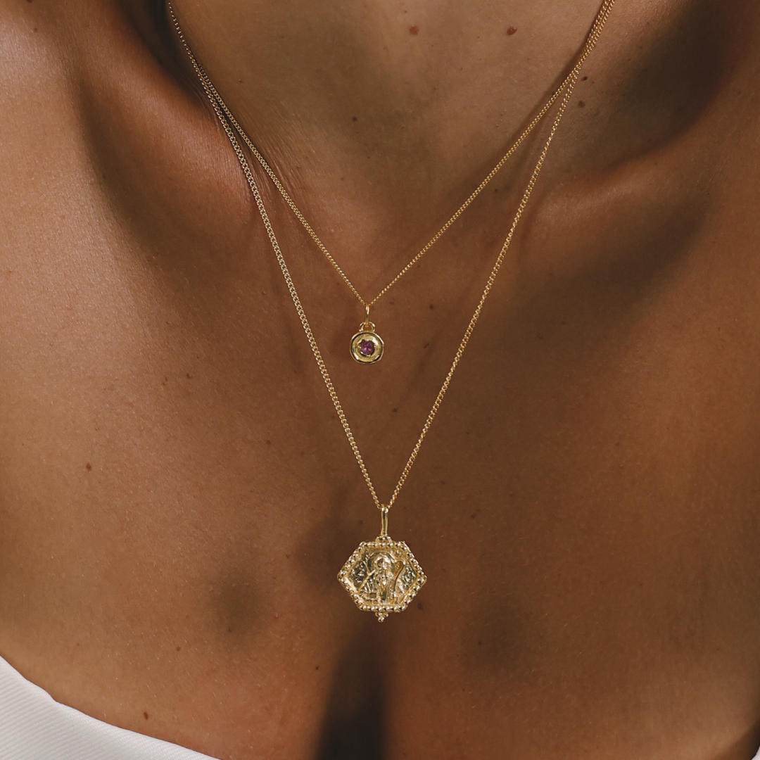 Close-up of a person wearing two gold necklaces with pendants.