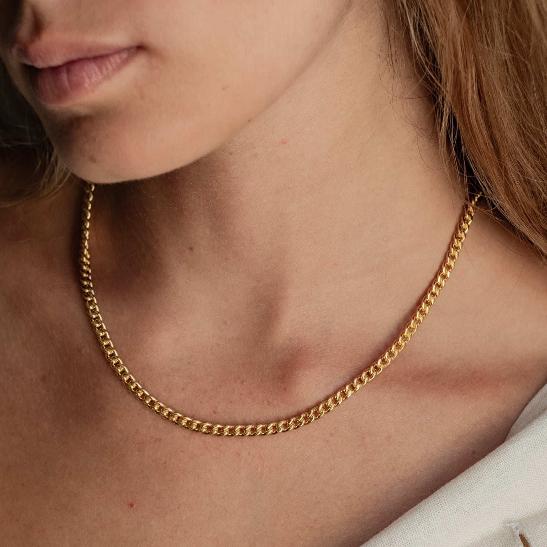Close-up of a woman wearing a single gold chain necklace with flat and interlocking links