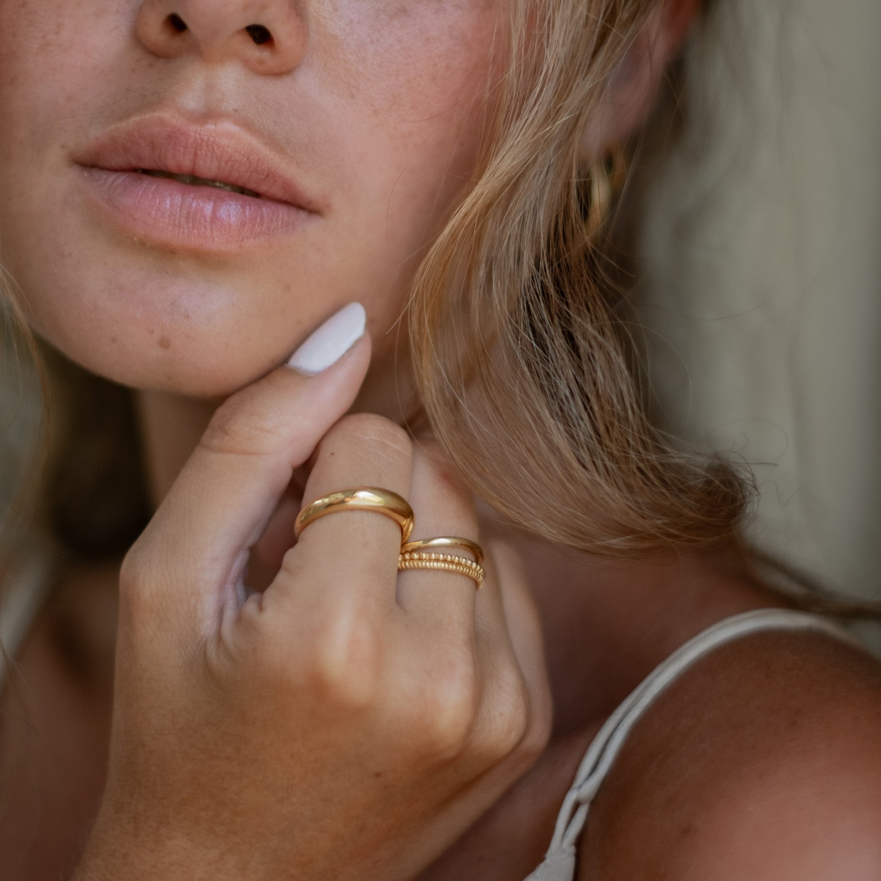 Close-up of a woman's face and hand, wearing gold rings with a polished finish.