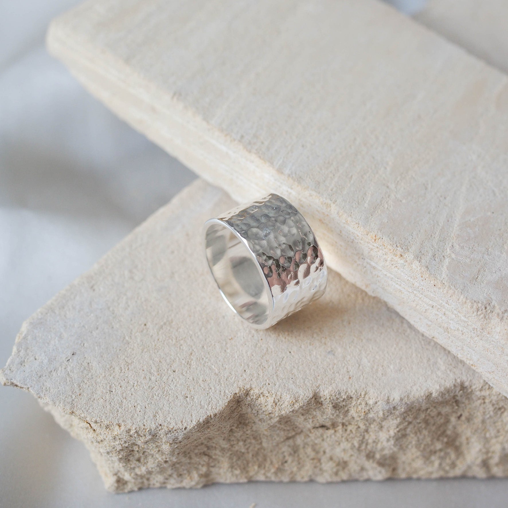 A single wide silver hammered ring on a beige stone.