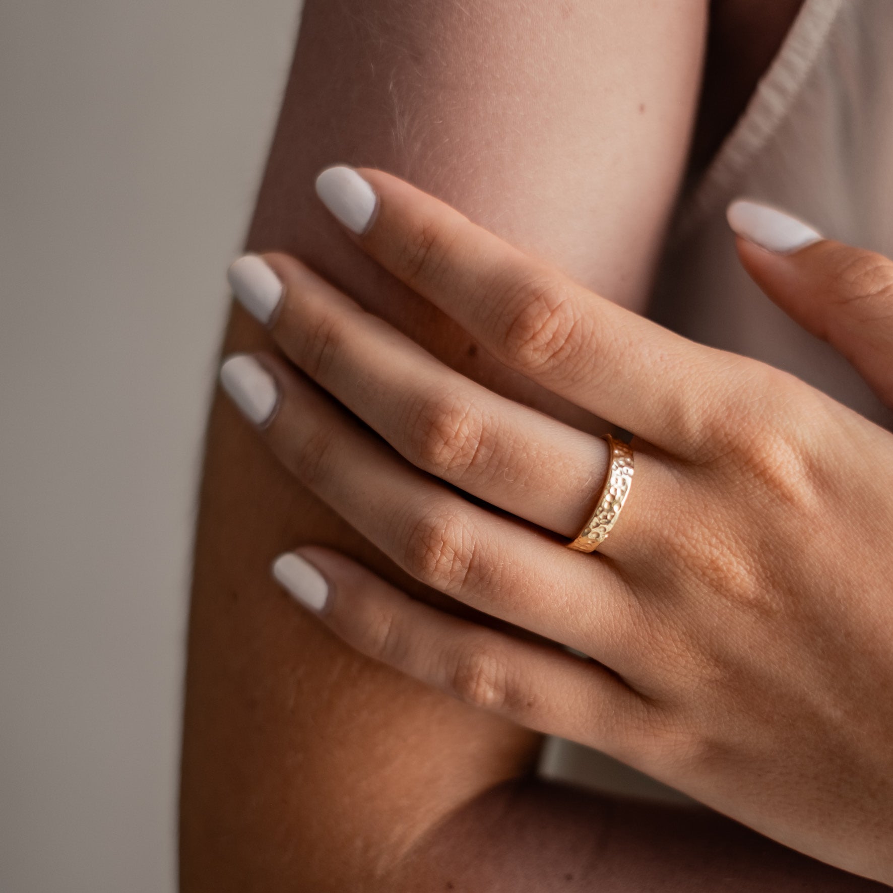 A close-up of a hand wearing a wide gold hammered ring.
