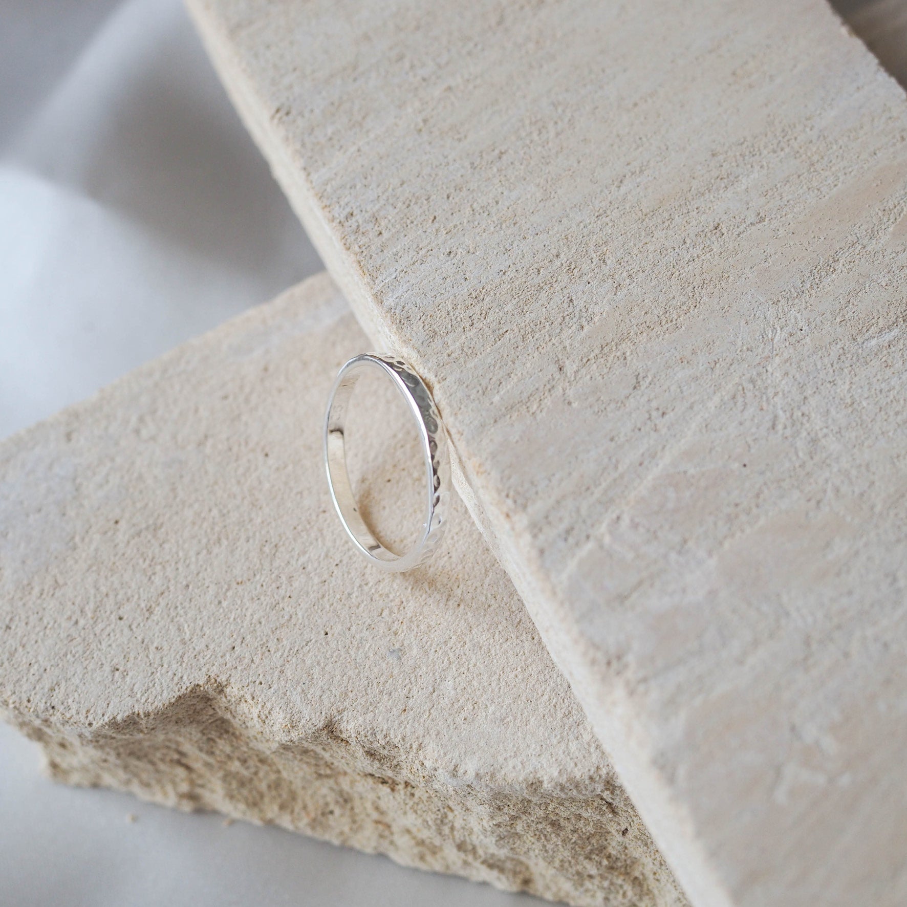 A single narrow, hammered silver ring on a beige stone.
