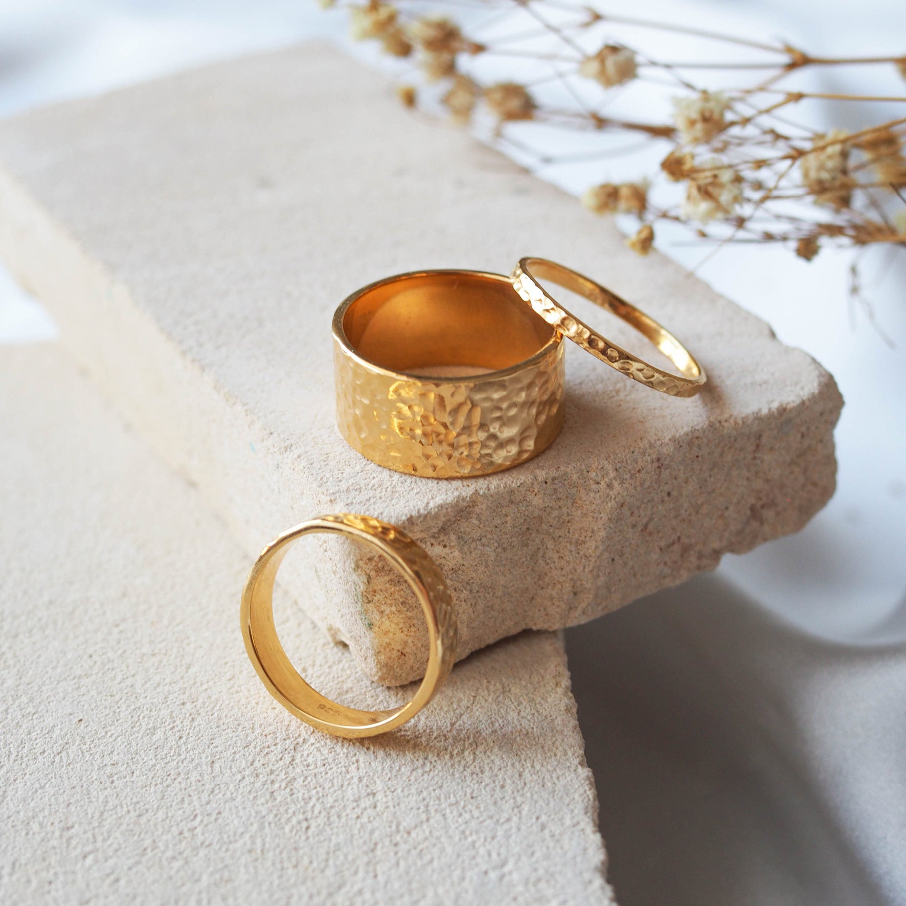 A set of three gold rings with a hammered texture on a beige stone.