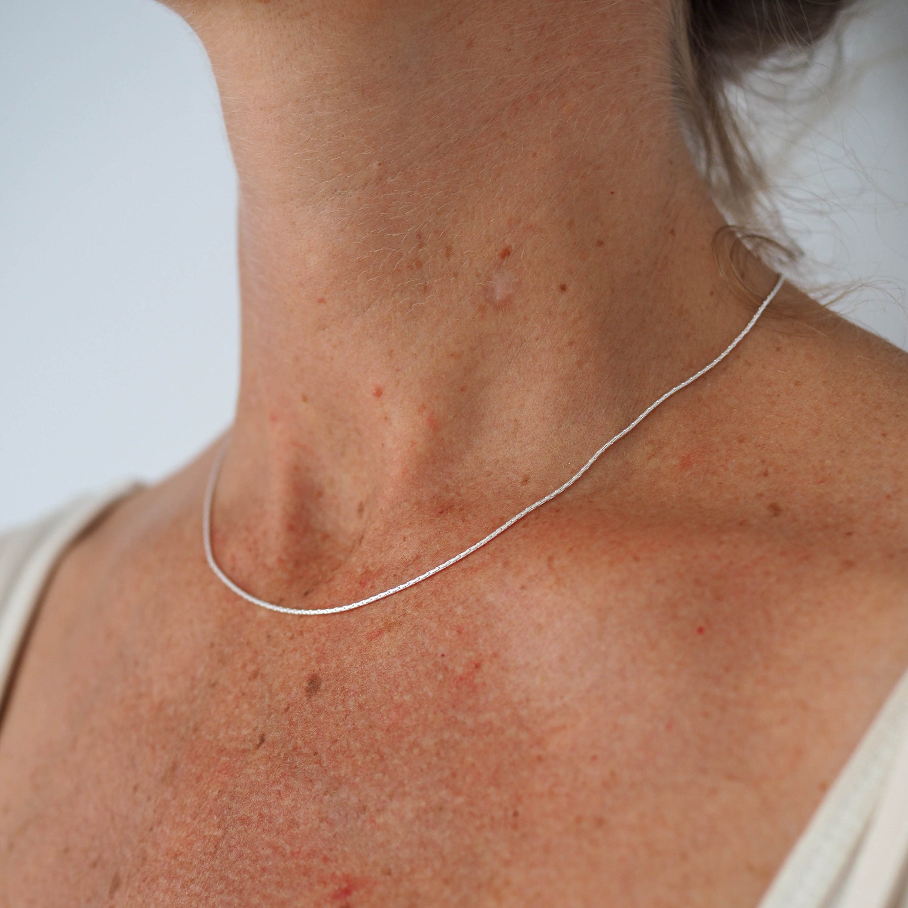 Close-up of a woman's neck wearing a thin silver chain necklace.