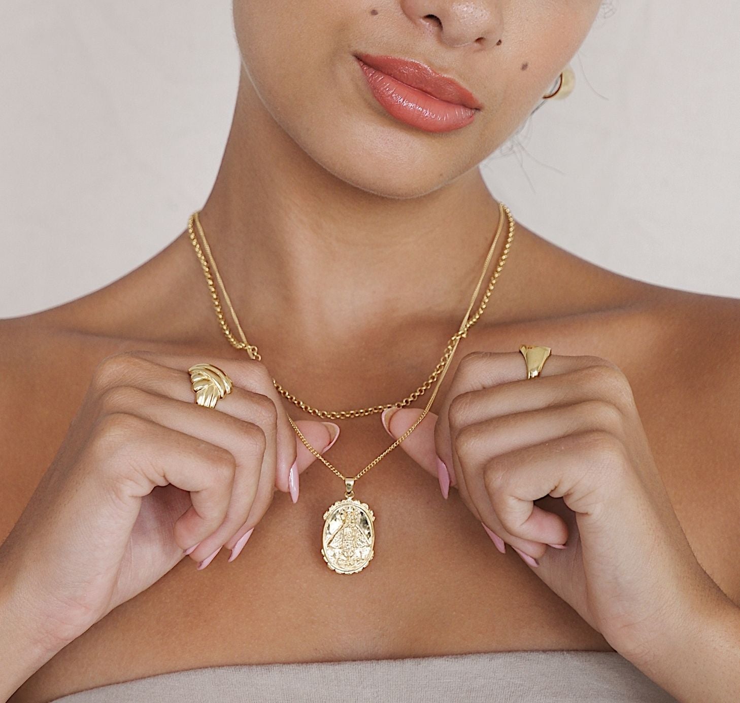 Woman wearing a gold necklace and rings on a plain background
