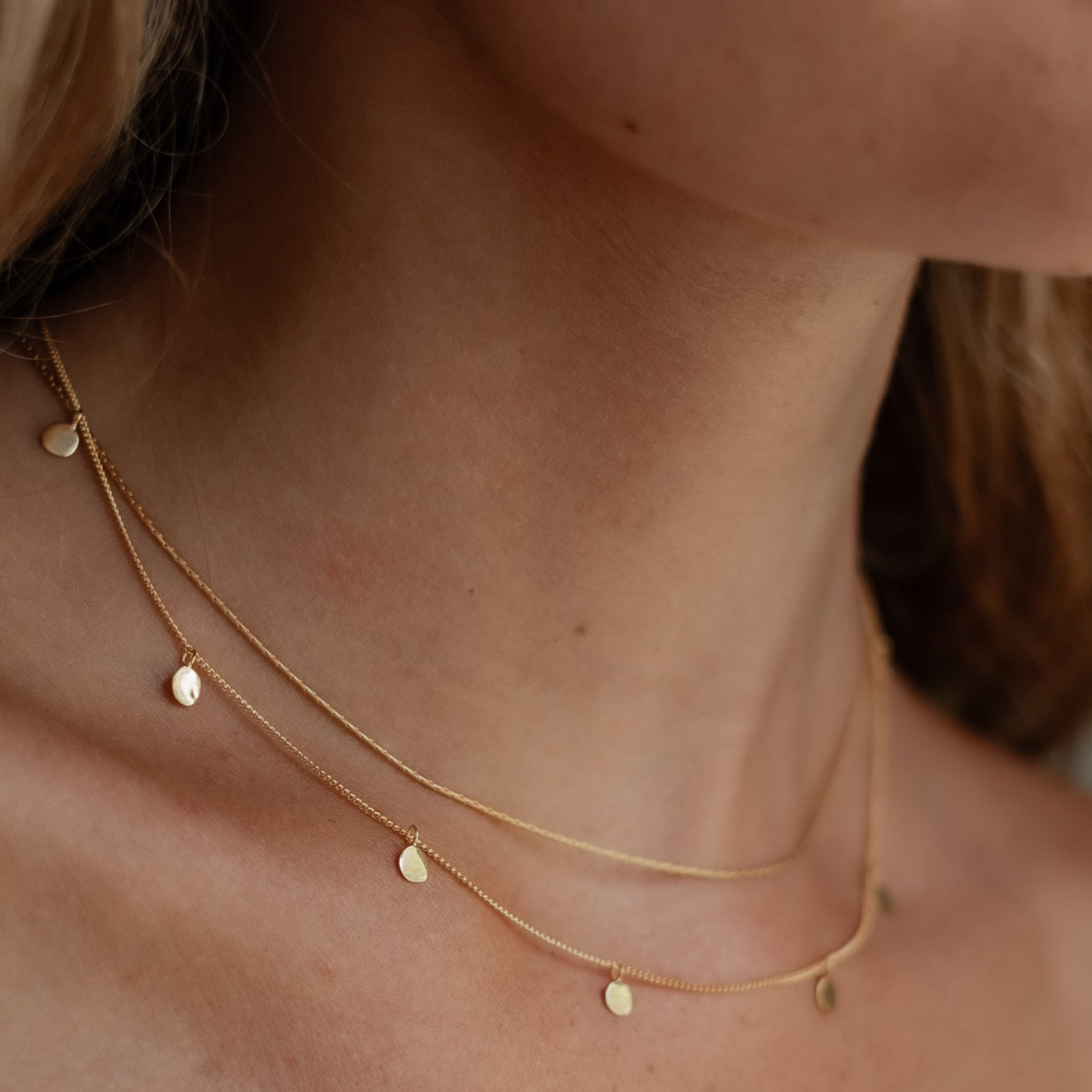 Close up of a woman wearing a gold necklace with small circular charms