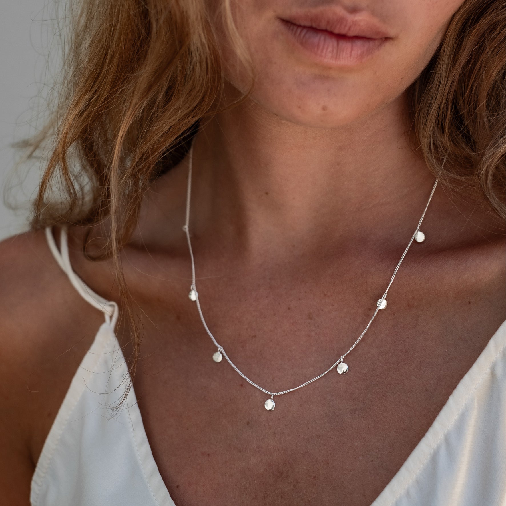 Close-up of a woman's neck and shoulders wearing a silver necklace