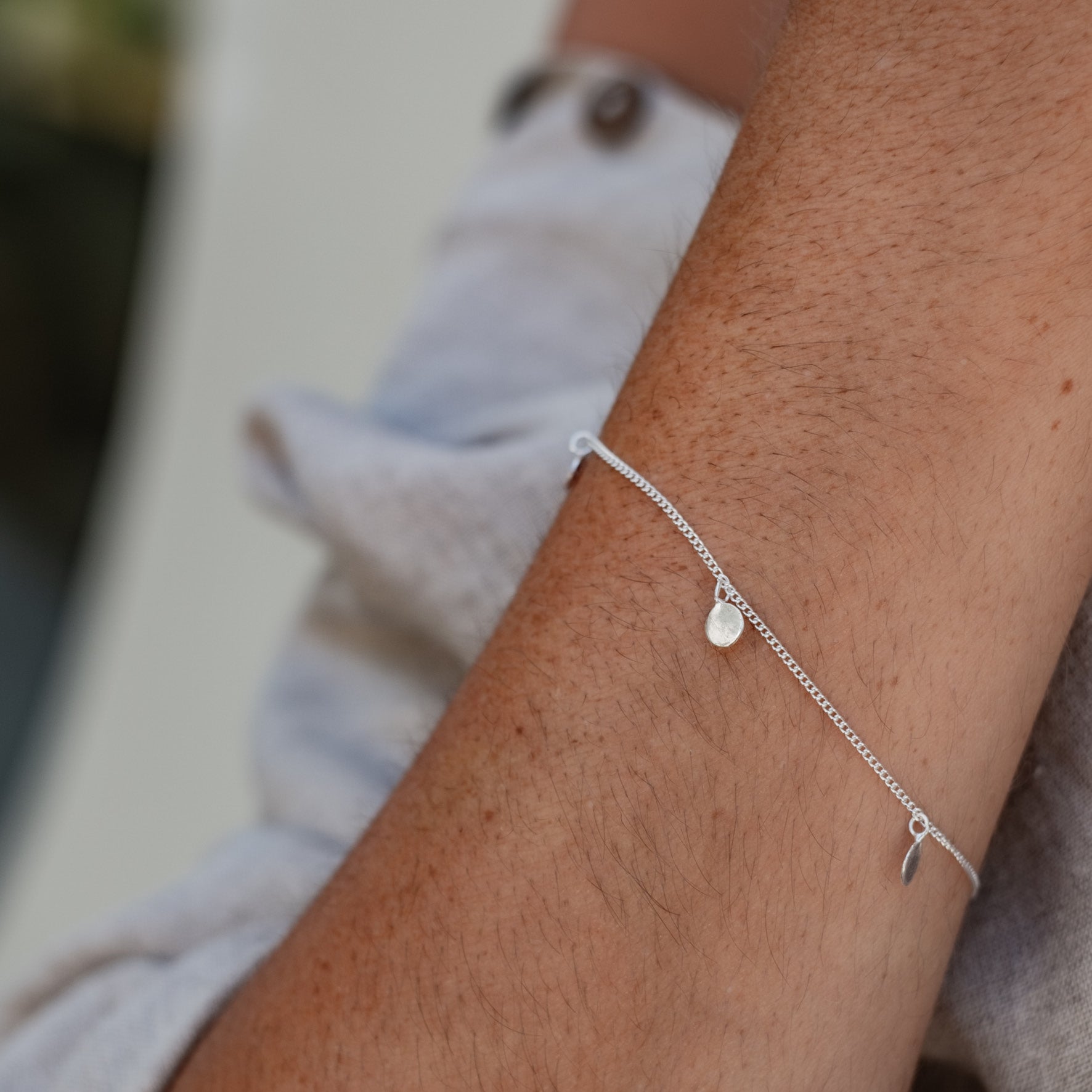 Close-up of a woman wearing a delicate silver bracelet with small circular charms.