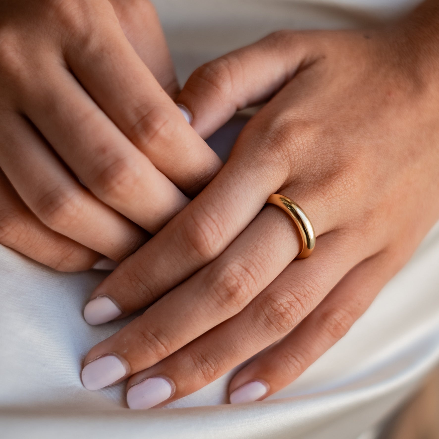Close-up of a woman's hands resting on her lap, showcasing a polished gold ring.
