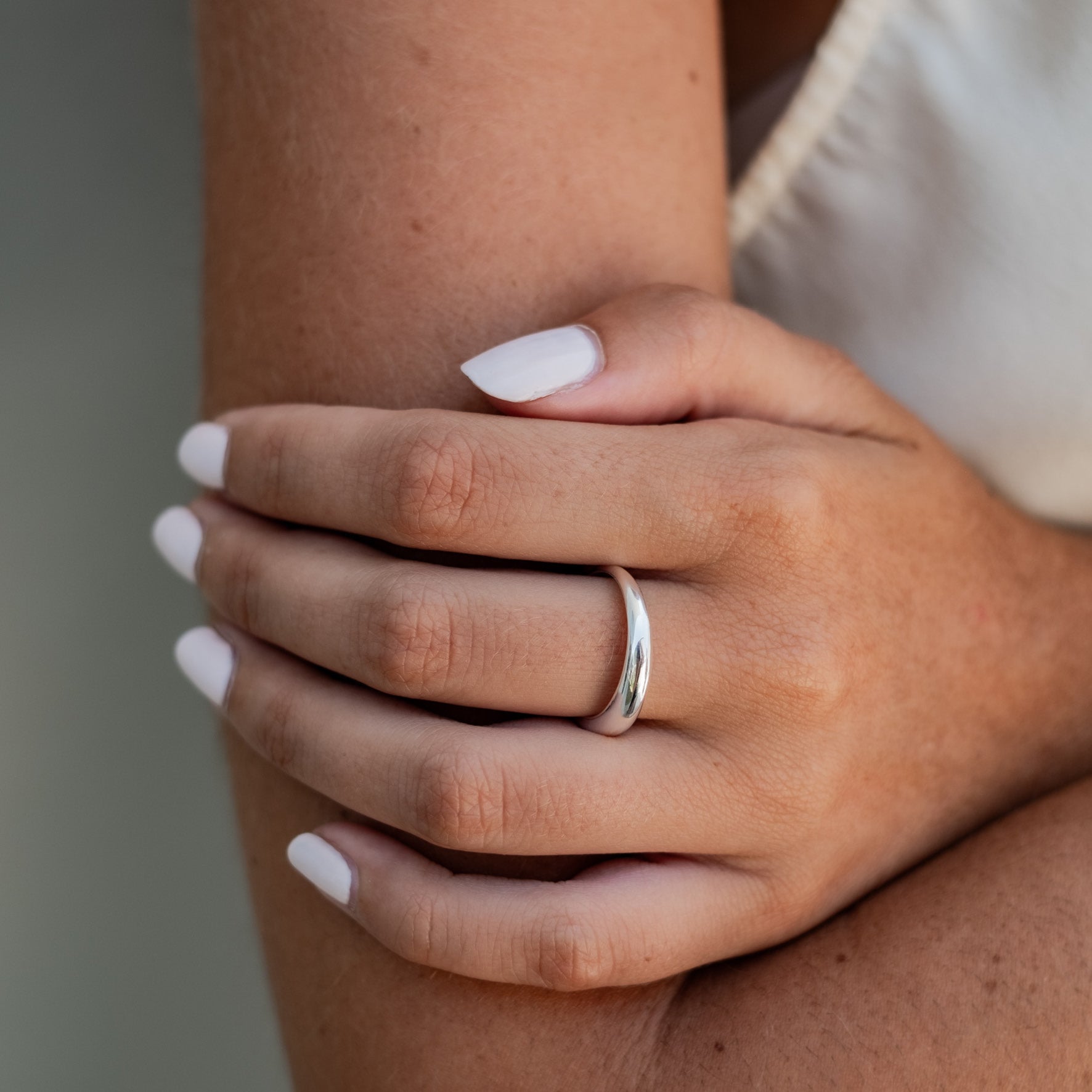 Close-up of a woman's hands resting on her arm, showcasing a polished silver ring.