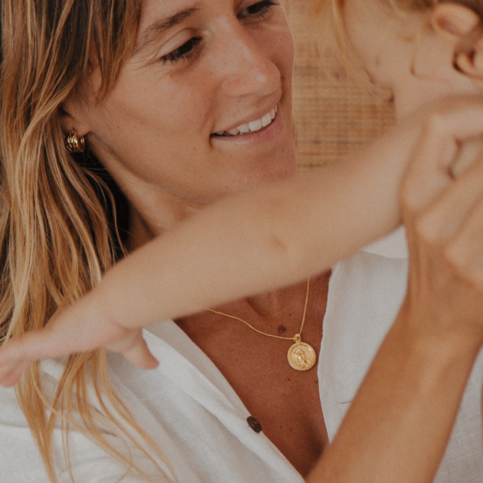 Woman with a child, both wearing gold jewelry, in a close and affectionate moment.