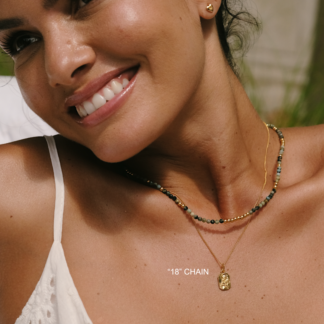 Woman wearing a gold necklace with a pendant outdoors