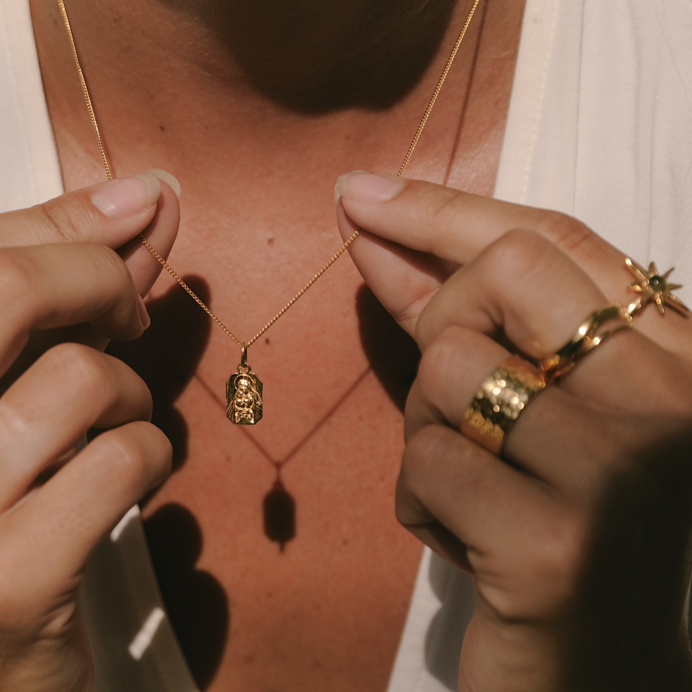 Close-up of hands adjusting a gold necklace with a pendant.
