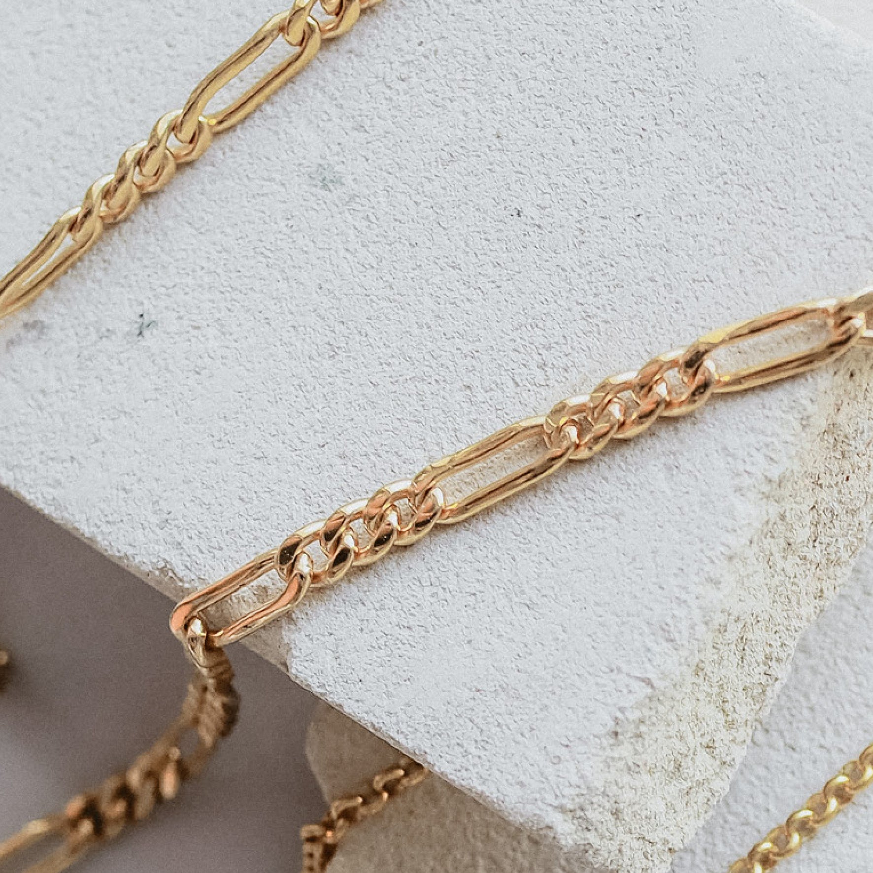 Close-up of a gold chain anklet resting on textured white stones.