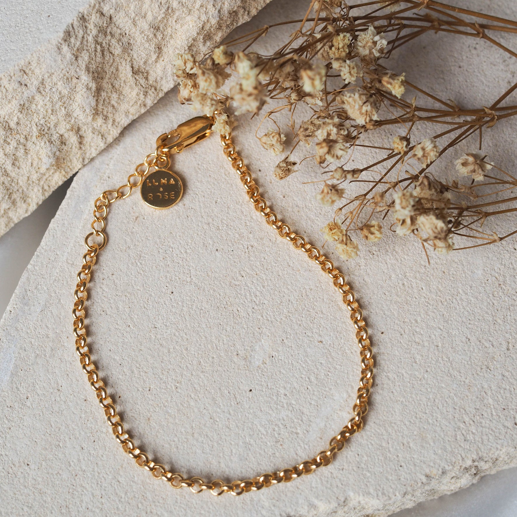 Close-up of a gold chain bracelet arranged on beige stone.
