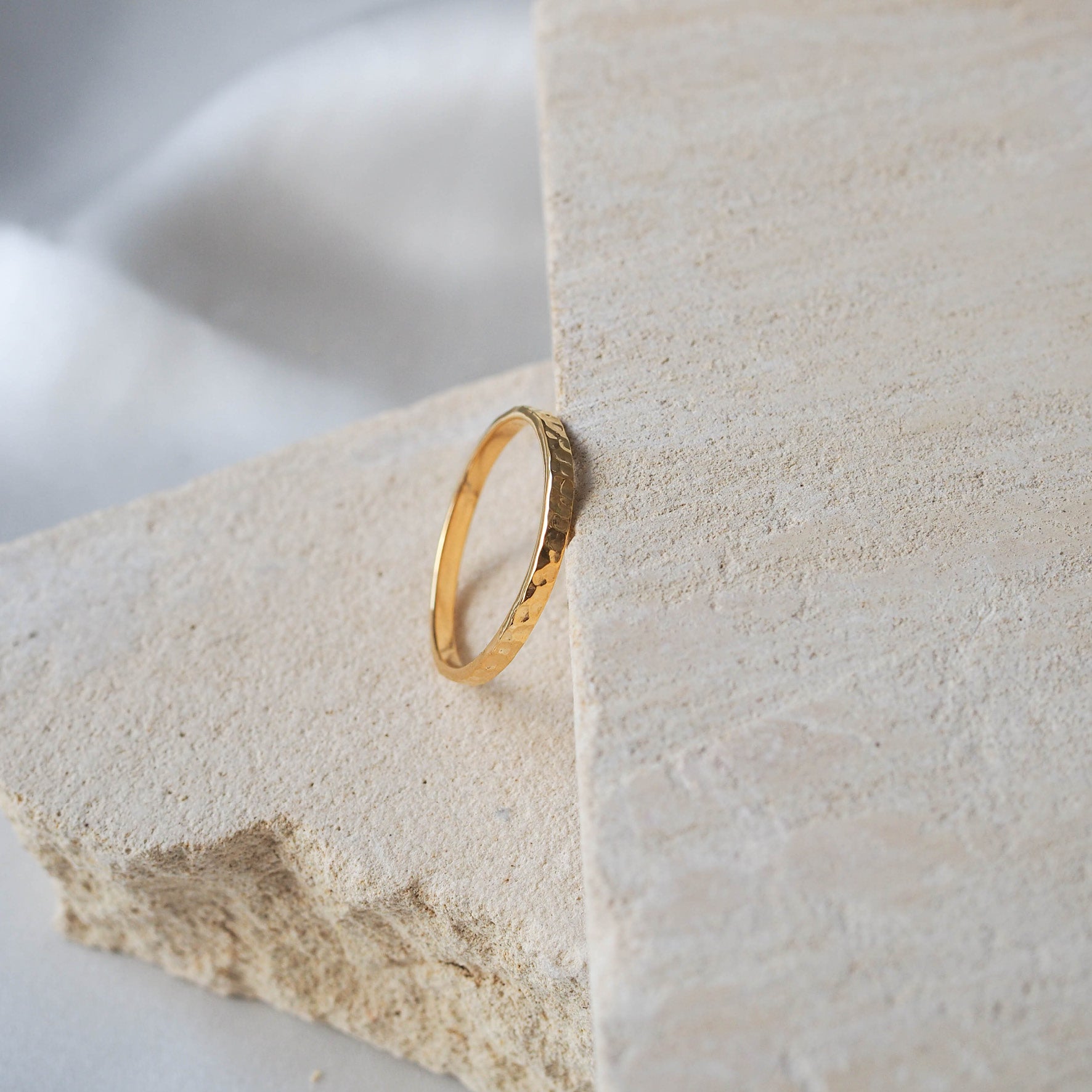 A thin gold hammered ring placed on a beige stone.