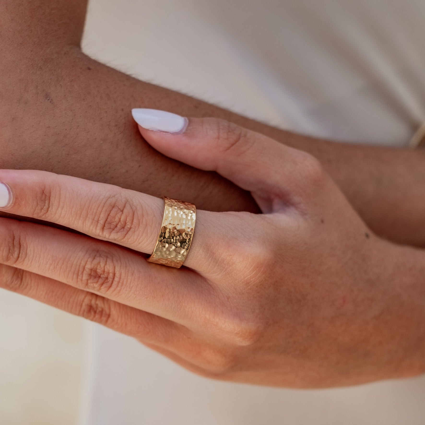 A close-up of a hand wearing a wide gold hammered ring.