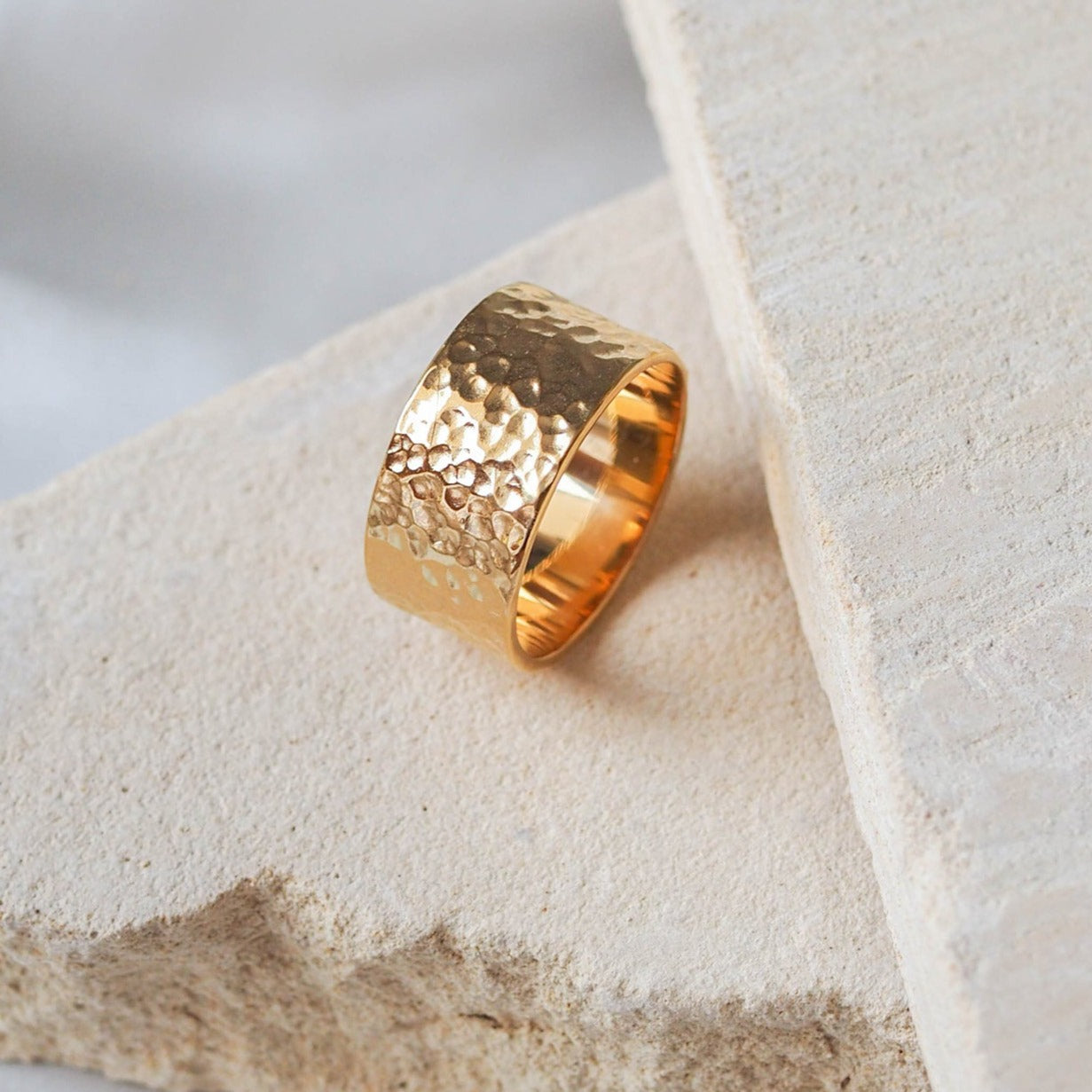 A single wide gold hammered ring on a beige stone.