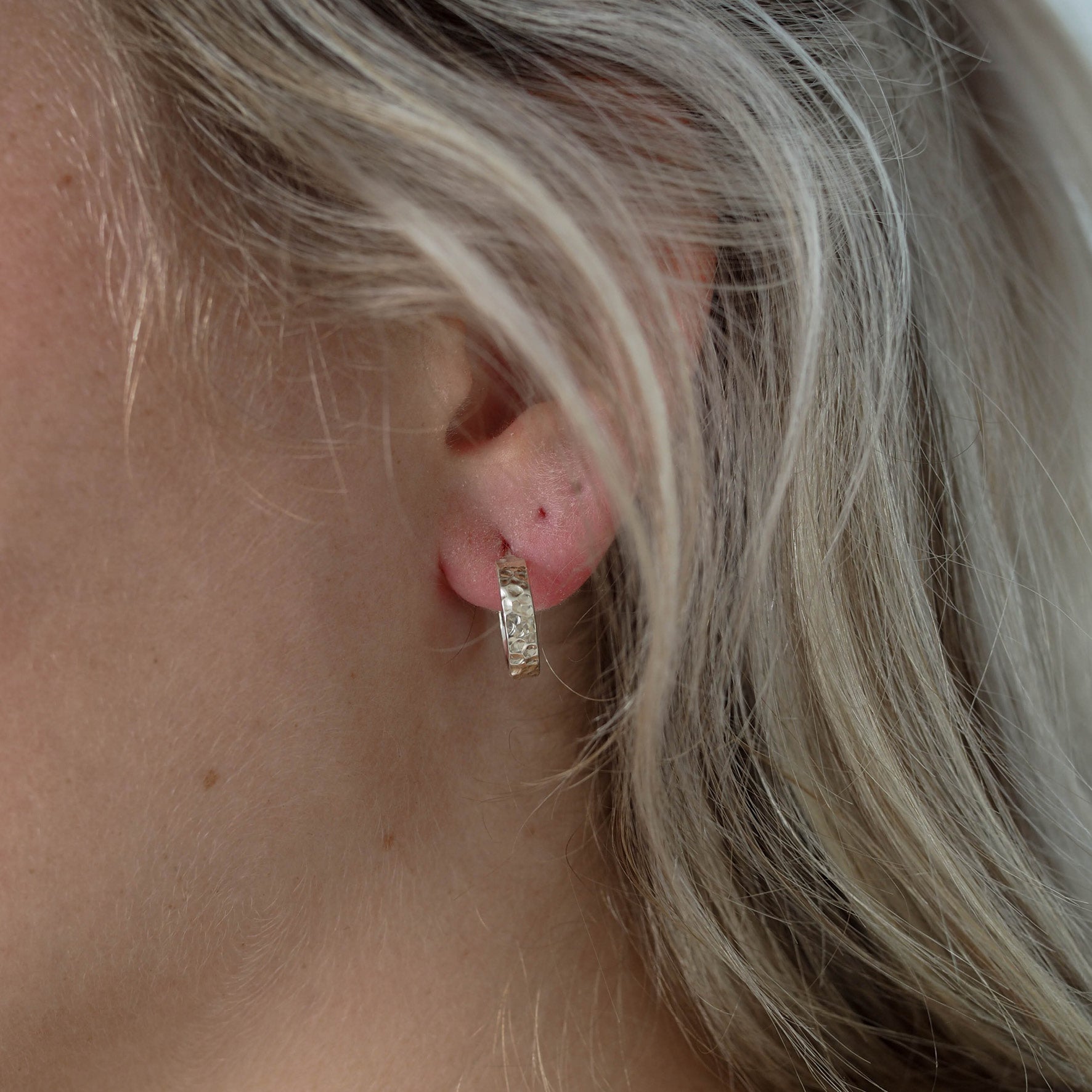 Close-up of a single hammered silver hoop earring worn on an ear with blonde hair.
