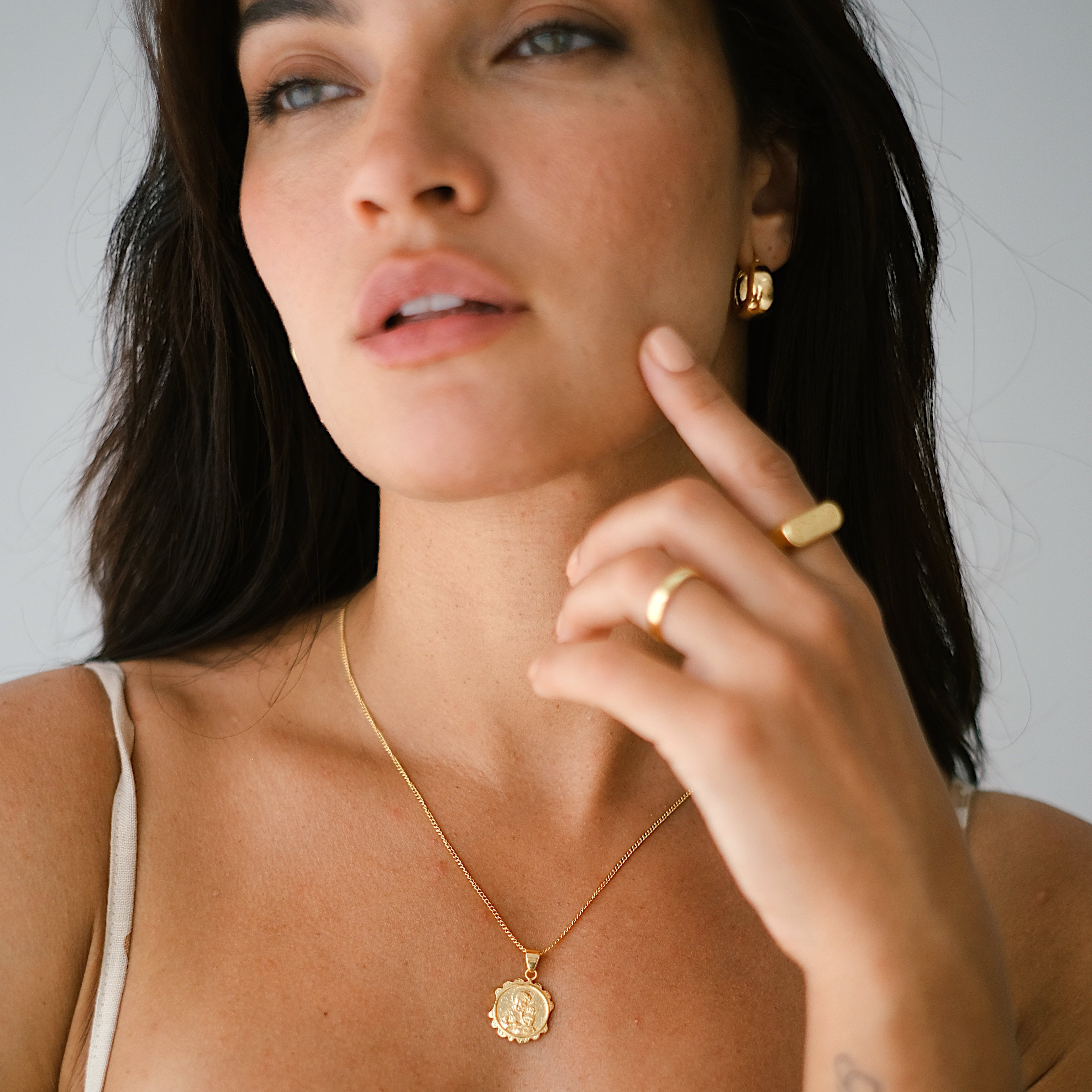 Woman wearing Gold necklace and Gold ring, Plain Gold earrings on a neurtral plain backdrop