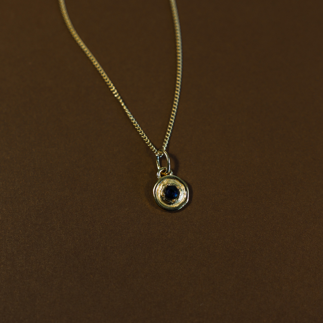 Gold necklace with a pendant featuring a blue gemstone on a brown background
