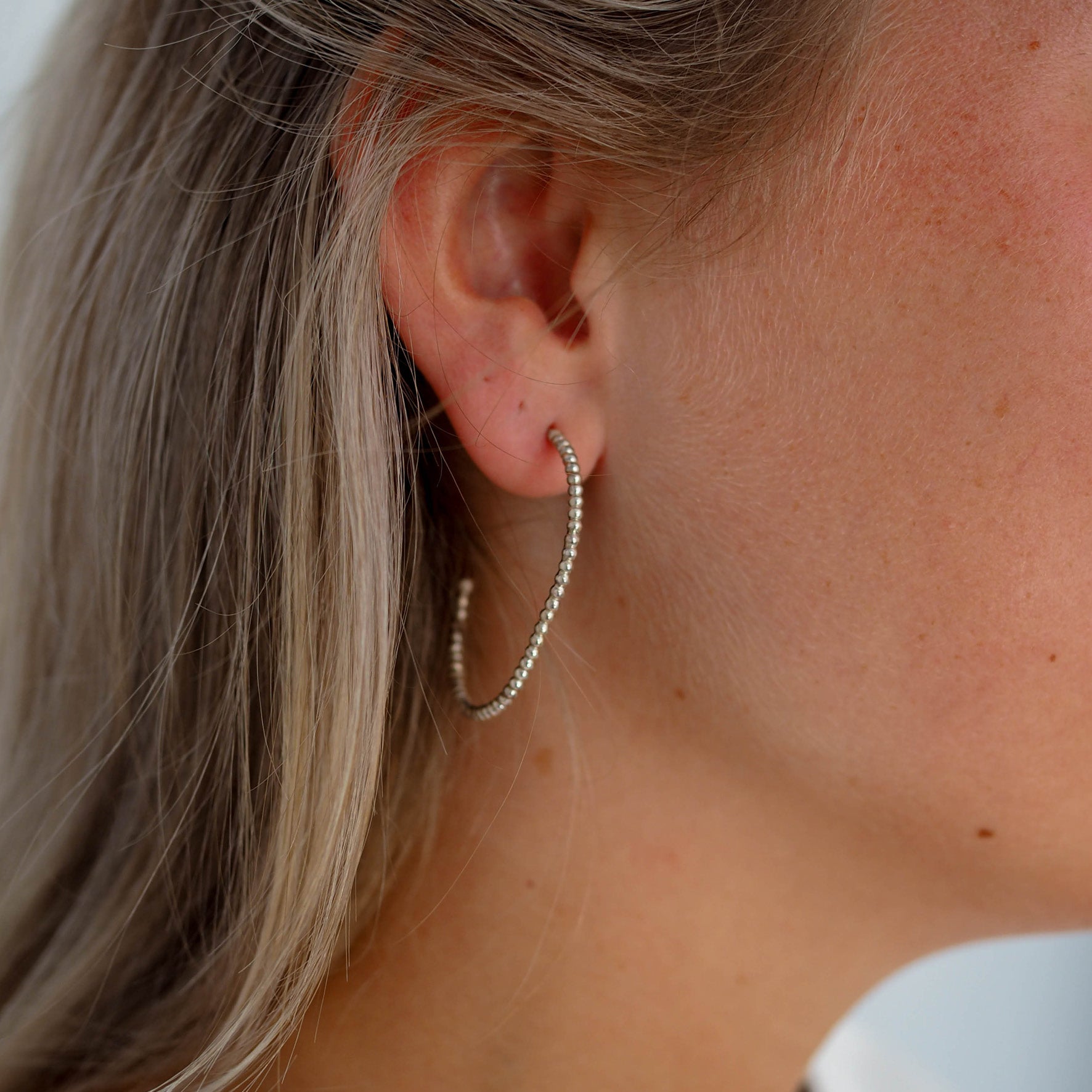 Close-up of a woman with blonde hair wearing a gold beaded earring