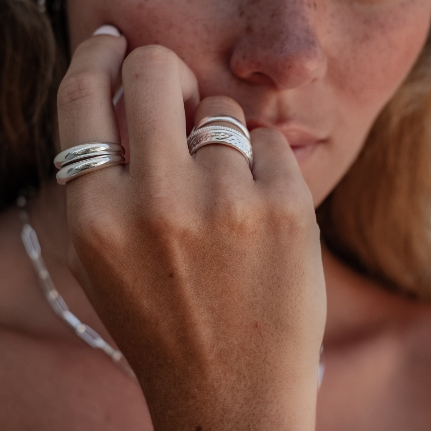 Close-up of a woman's face and hand, wearing silver rings with a polished finish.