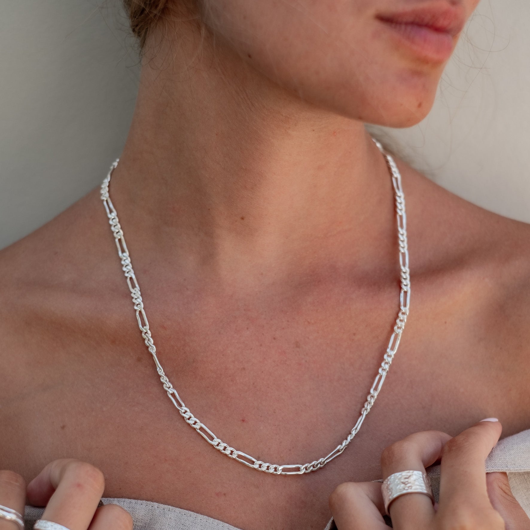 A woman wearing a silver chain necklace and a wide silver ring, shown from the shoulders up.