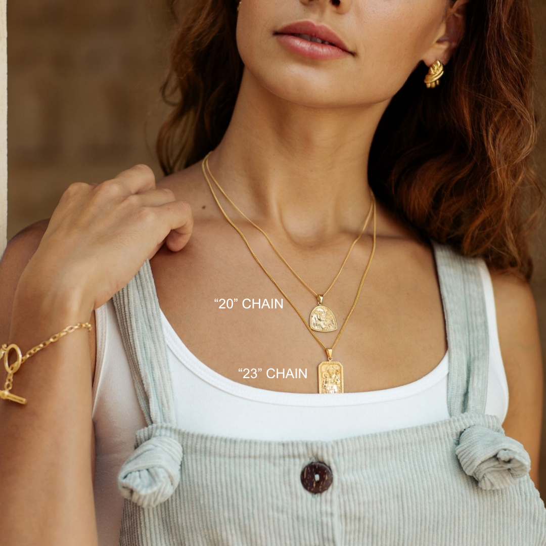 Woman wearing gold necklaces with labeled chain lengths, wearing a white top and light overalls.