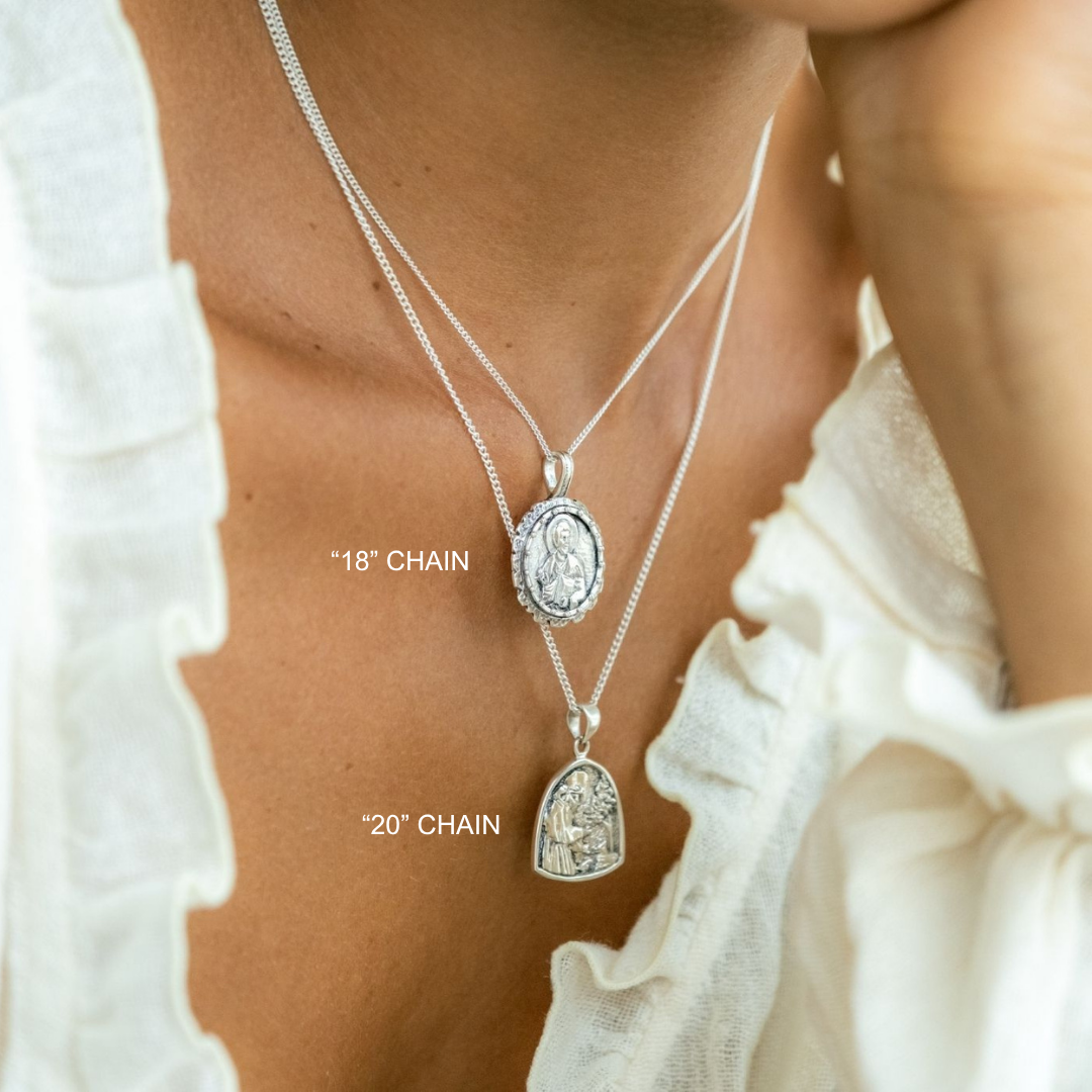 Silver necklaces with pendants on a person wearing a white top.