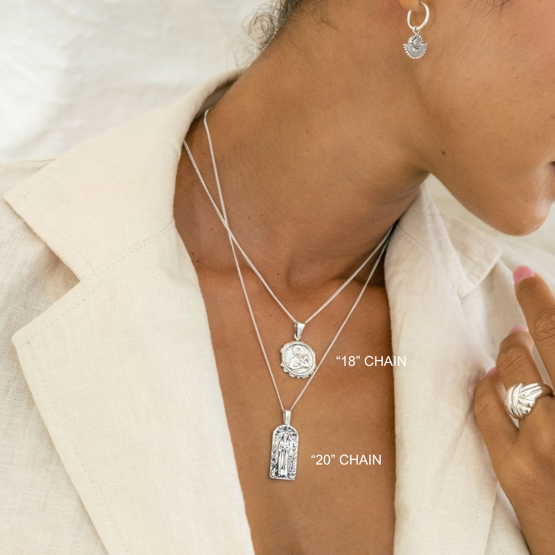 Silver necklaces with pendants on a person wearing a beige jacket.