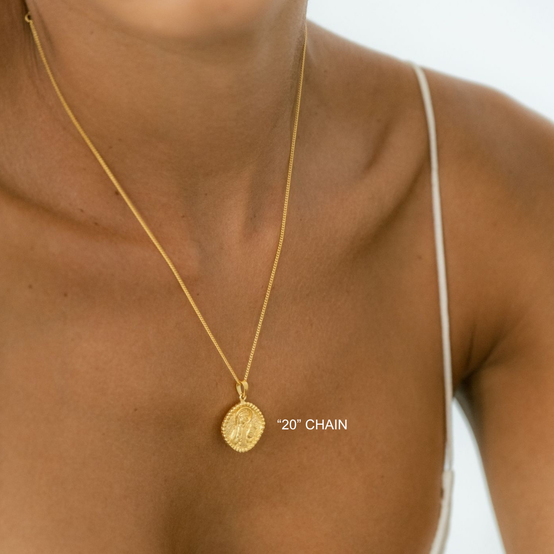 Gold necklace with a pendant on a person's neck against a neutral background