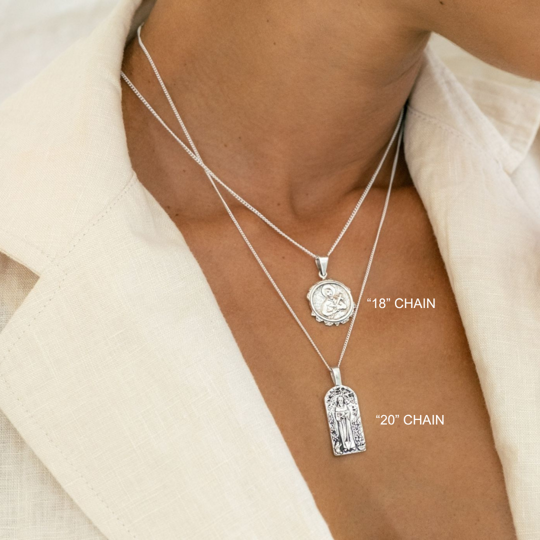 Two silver necklaces with pendants on a person wearing a cream jacket.