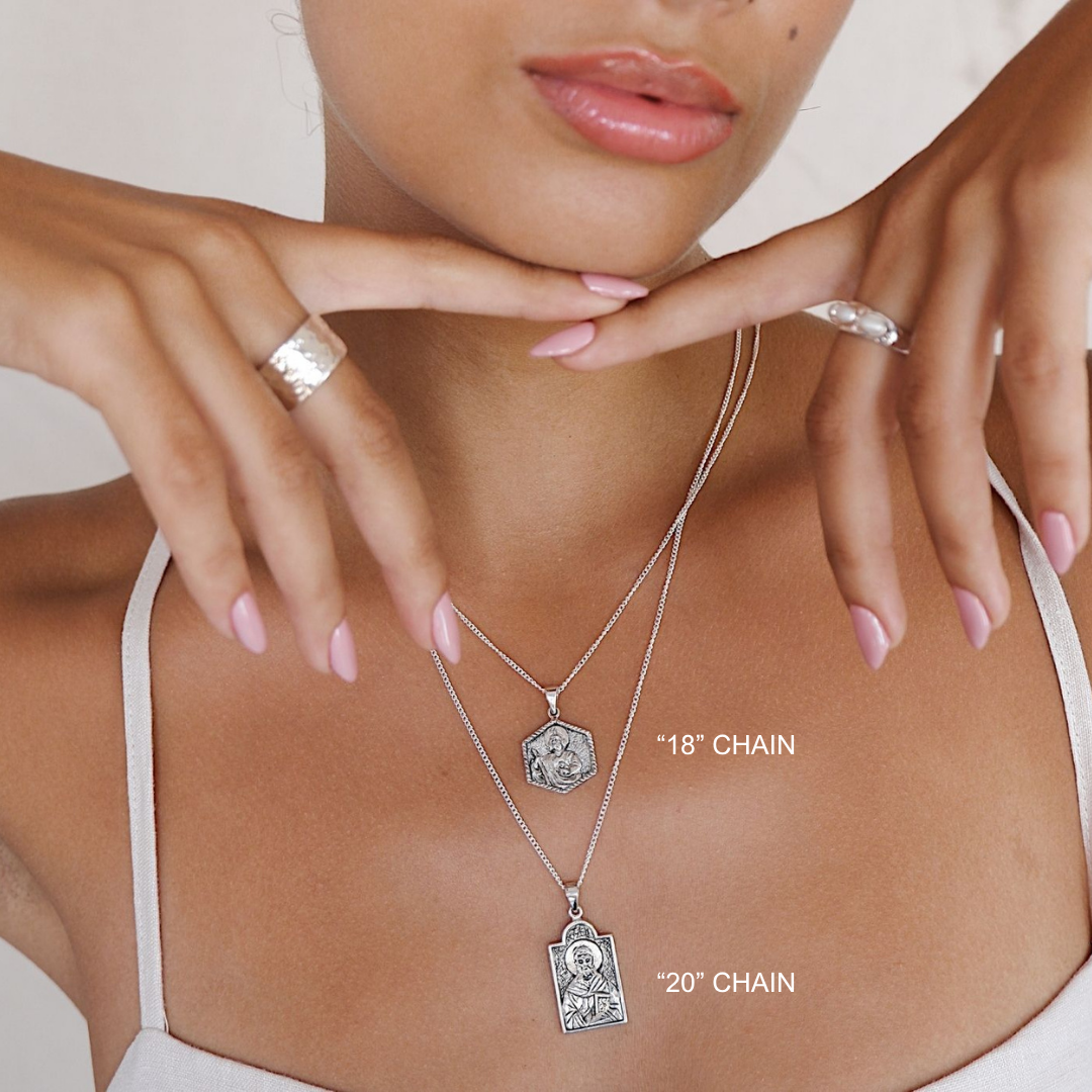 Close-up of a person wearing two silver necklaces with chains labeled '18' and '20', with a neutral background.