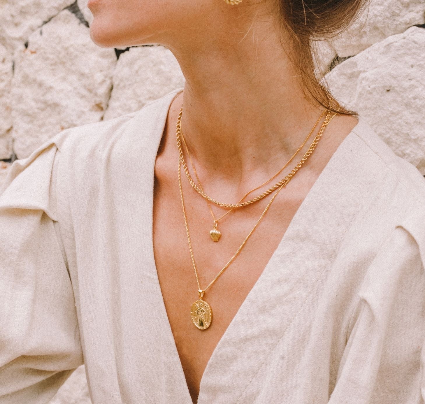a woman wearing three necklaces gold