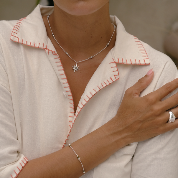 Woman wearing a white outfit with pink trim, jewelry, and a blurred background