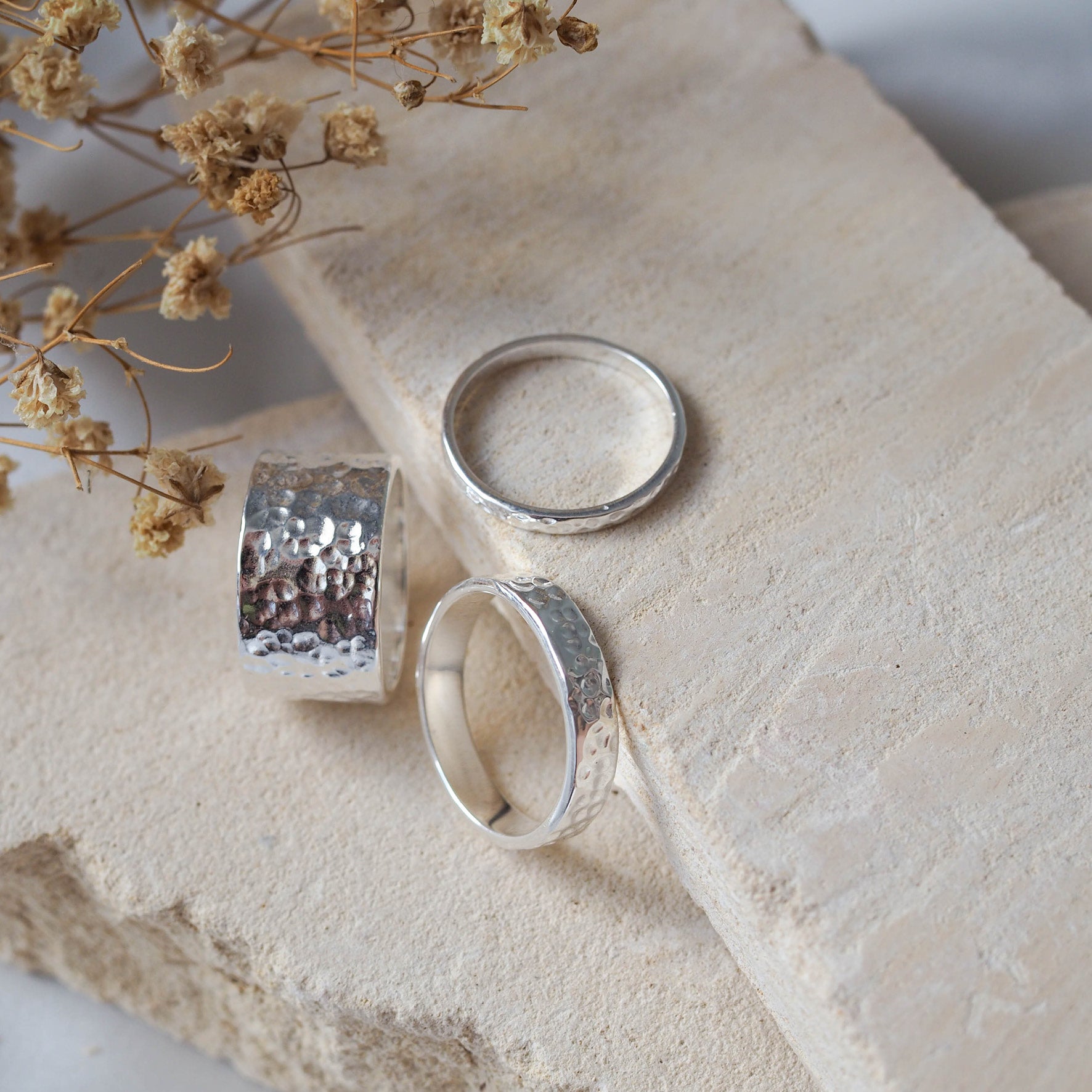 A set of three silver rings with a hammered texture on a beige stone.