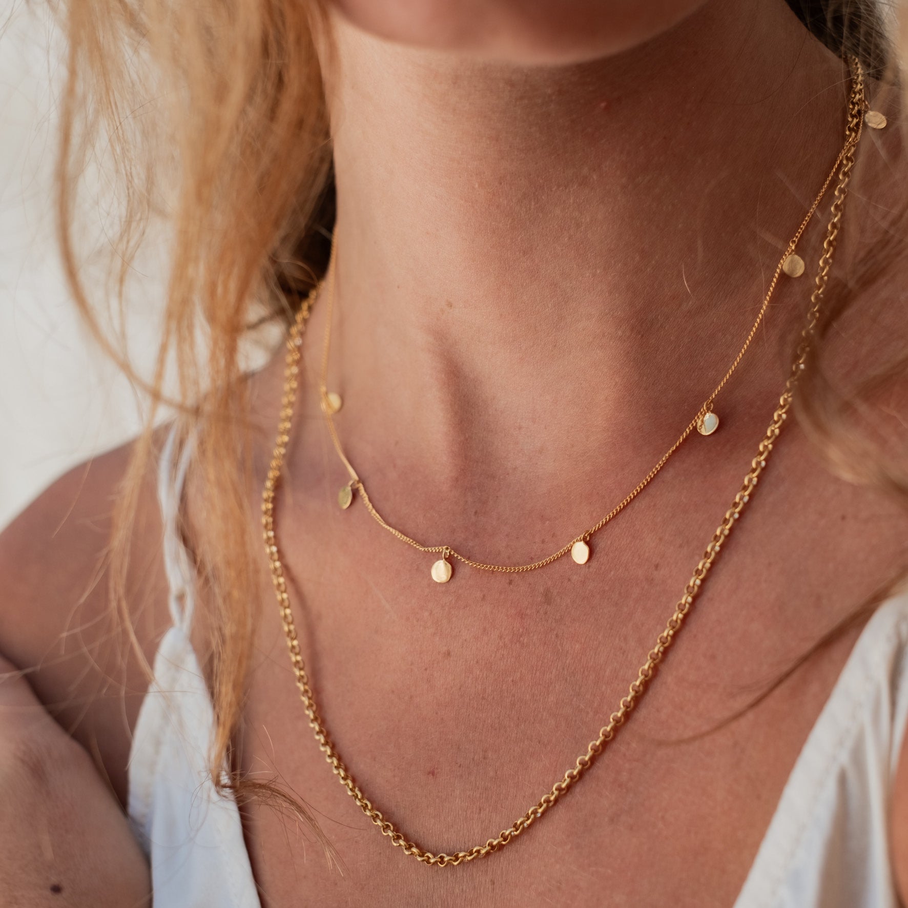 Close-up of a woman's neck and shoulders wearing layered necklaces