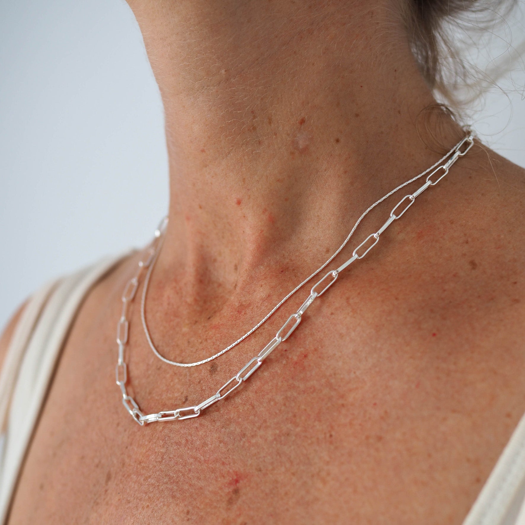 Close-up of a woman's neck wearing a thin silver chain necklace and silver link necklace.