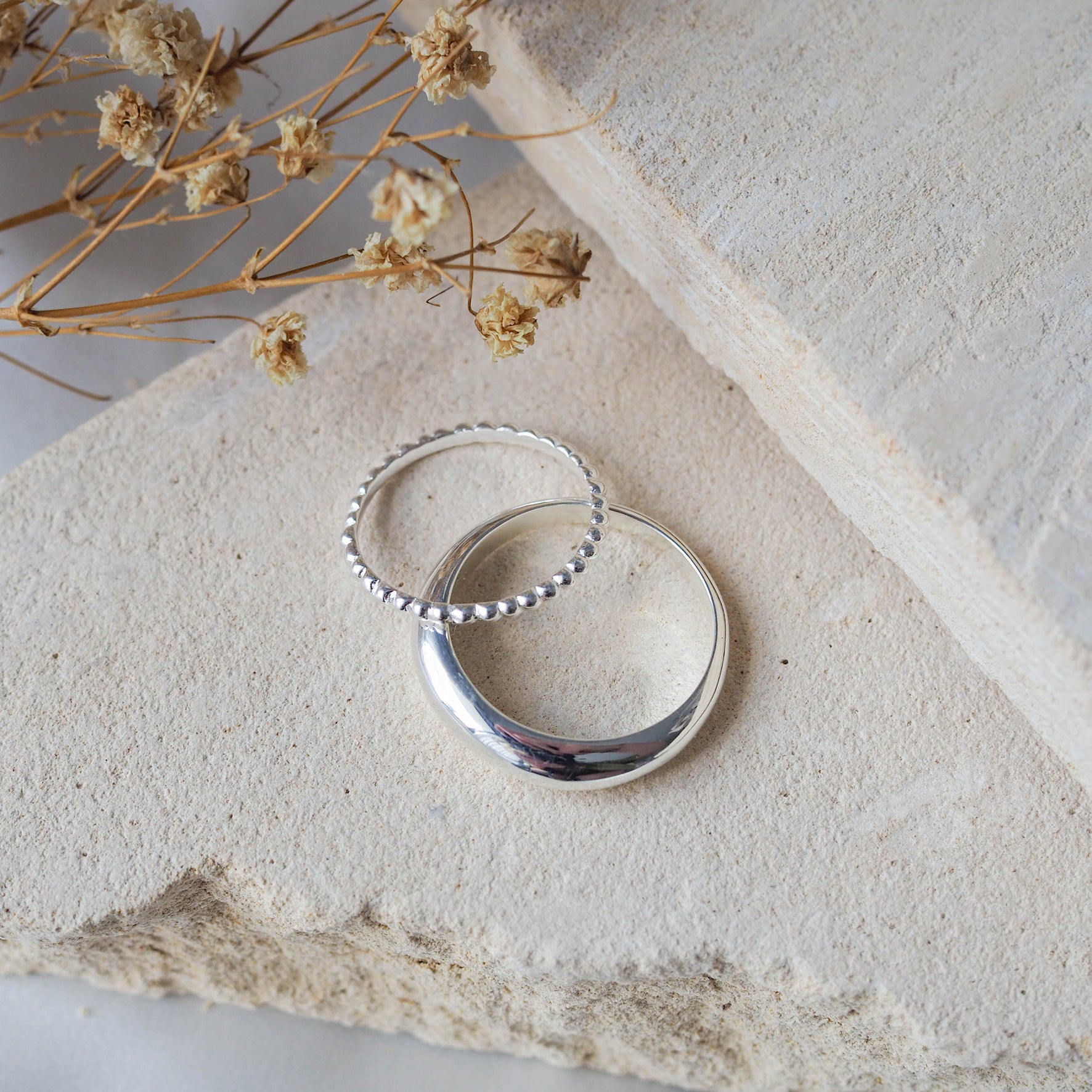 Close-up of a polished silver ring displayed on beige stone.